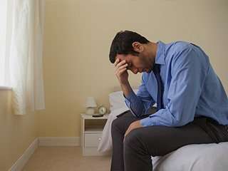 Sad man with head in hand in bedroom