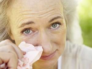 Woman wiping her irritated eyes with a tissue