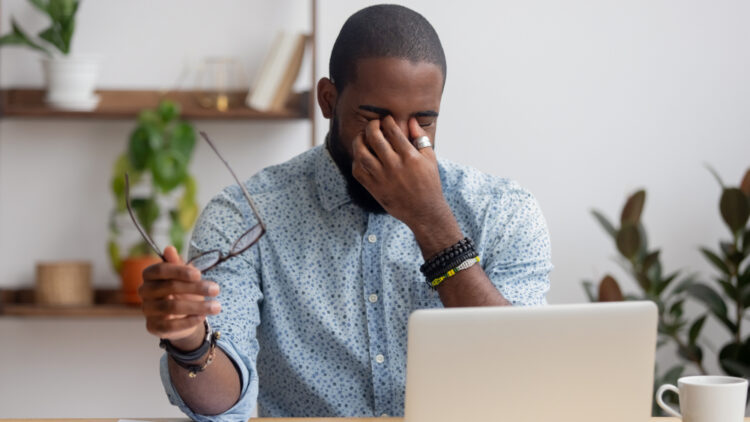 Man rubbing eyes in pain while working on a laptop