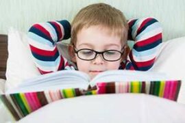 Little boy with glasses reading in bed